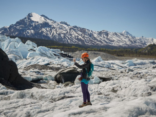 A blonde adult female female hiker takes a cell phone photograph