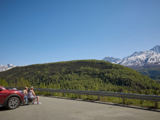 An older male and female sit next to their car overlooking the M